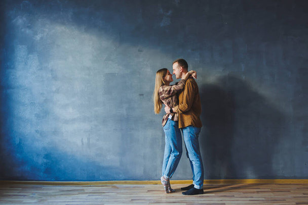 Sonriente feliz pareja vestida con jeans y camisas de pie sobre un fondo de pared gris, aislado fondo de pared de hormigón gris. El concepto de una pareja feliz enamorada. - Foto, Imagen