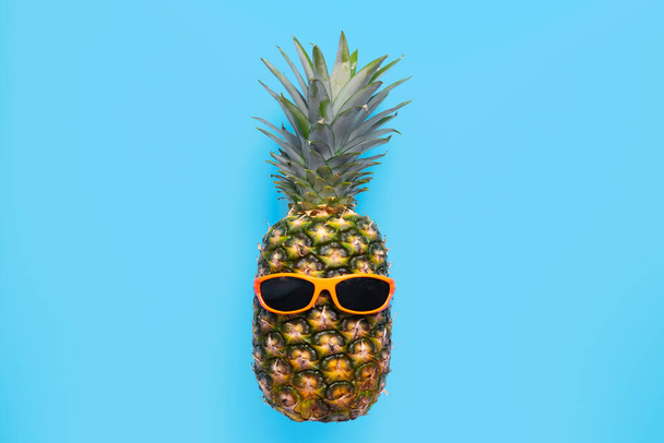 Ananas w okularach przeciwsłonecznych na niebieskim tle. - Zdjęcie, obraz