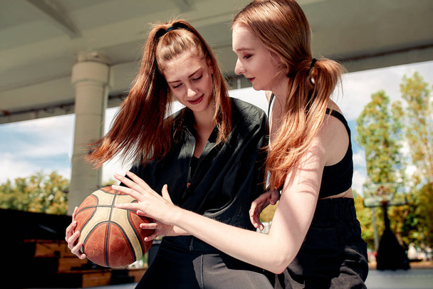 Two young women show togetherness and friendship as they share a moment over a basketball. - Fotoğraf, Görsel