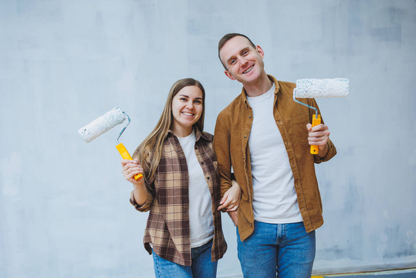 A young married couple in love paints the walls with white paint using rollers. Renovation in the apartment of a happy couple - Foto, Imagen