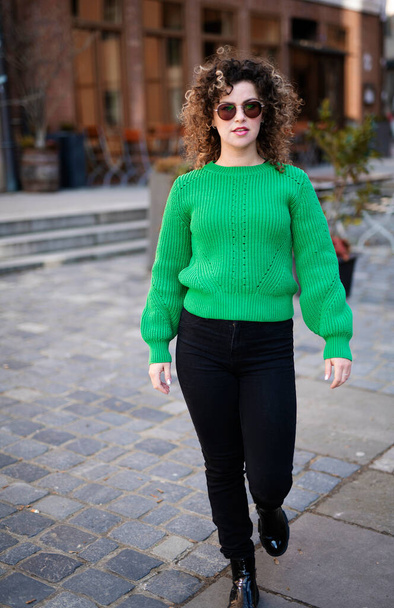 Mulher na moda jovem em uma camisola verde anda pela cidade, conceito de moda de rua - Foto, Imagem