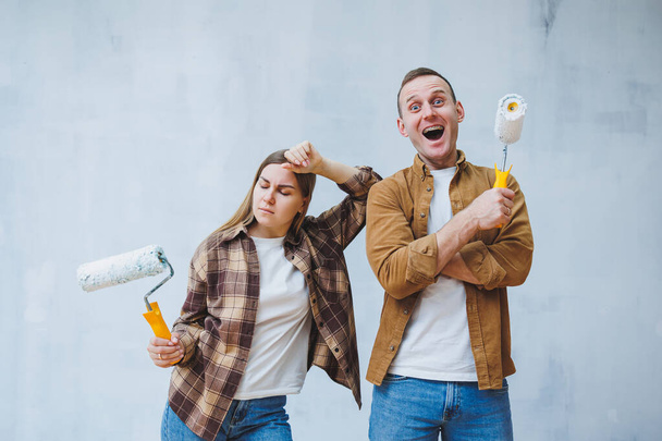 Happy young married couple in love in shirts doing renovations, renovating walls painting with white paint roller, preparing to move into new house, selective focus. - Foto, Imagen