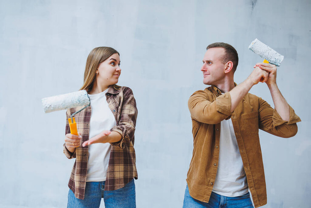 Happy young married couple in love in shirts doing renovations, renovating walls painting with white paint roller, preparing to move into new house, selective focus. - 写真・画像