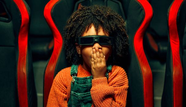 Une fille mignonne afro-américaine avec et un garçon caucasien mignon assis dans un cinéma virtuel à lunettes sur des chaises tournantes mobiles et regardant émotionnellement un film dans un parc d'attractions. - Photo, image