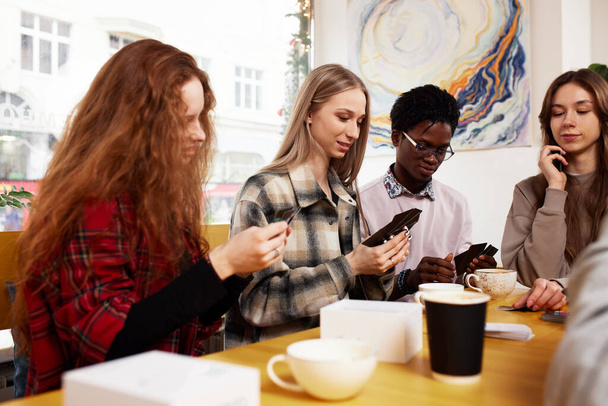Una empresa multinacional de jóvenes bebe café y juega juegos, mira teléfonos inteligentes, toma selfies - Foto, imagen