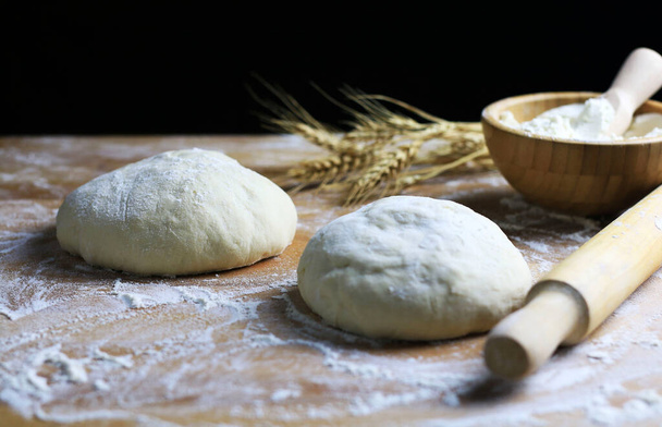 Homemade pasta dough ready for cooking and wheat ears on a floured wooden table. Black background. Copy space. - Foto, imagen
