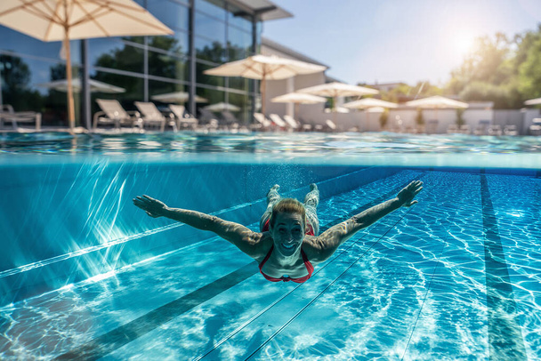ホテルやスパのリゾートでスイミングプールで泳いでいる女性の写真の上と水中  - 写真・画像