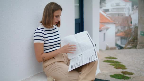 Gyönyörű lány nézegeti az újságokat az utcán. Fókuszált utazó kávét iszik és helyi híreket olvas a nyári vakációról. Gondtalan nő élvezi a délelőttöt egyedül az európai úton. Tavaszi utazás szabadidő. - Felvétel, videó