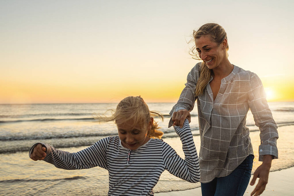 Kumsal tatilindeki mutlu anne ve kız. Anne ve küçük kızı yaz günbatımında sahilde birlikte yürüyüp oynuyorlar. Mutlu aile seyahatleri ve tatil konsepti imajı.  - Fotoğraf, Görsel