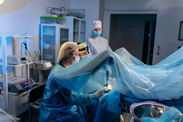 Squadra professionale di chirurghi proctologo che esegue l'operazione utilizzando dispositivi medici speciali in sala operatoria in ospedale. Concetto chirurgico urgente - Foto, immagini