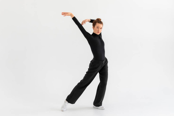 Menina jovem, dançarina de hip-hop profissional em uma roupa preta que executa sobre um fundo branco isolado com uma abundância de espaço de cópia. - Foto, Imagem