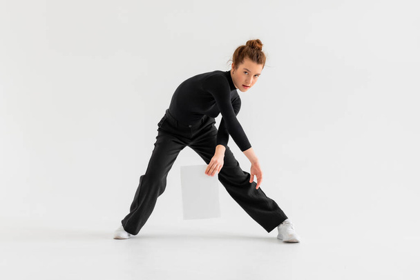 Young Girl, professional hip-hop dancer in a black clothes with blank white paper in the hand and performing over a Isolated white background with a plenty of copy space. - Valokuva, kuva