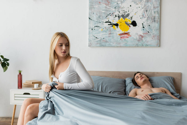blonde woman pulling blanket while shirtless man sleeping after one night stand   - Photo, Image
