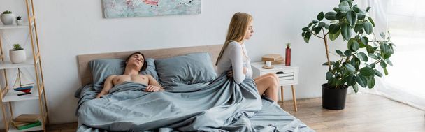 disappointed woman sitting on bed near shirtless man after one night stand, banner  - Photo, Image