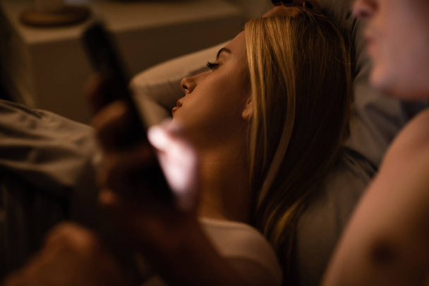 blonde woman sleeping next to unfaithful man with smartphone, cheating concept  - Foto, immagini