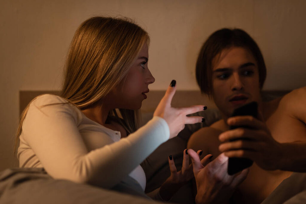 mujer rubia haciendo gestos mientras discute con su novio por la noche, concepto de engaño  - Foto, imagen