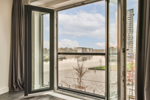 una habitación con una vista del agua desde su ventana que canta a la calle y los edificios en la distancia - Foto, imagen