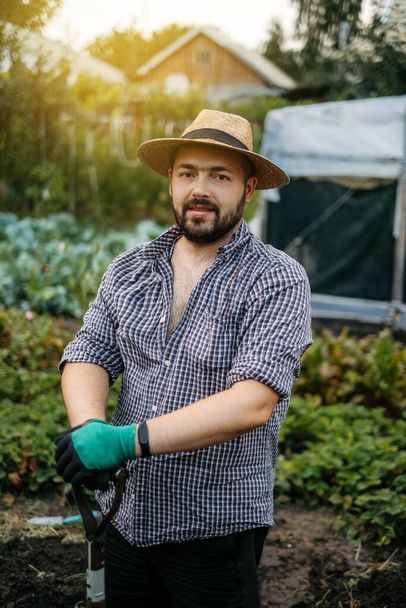 Un agriculteur coiffé d'un chapeau et d'une chemise à carreaux sourit dans le jardin. Paysan avec une barbe - Photo, image