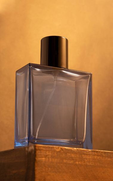 Een lege blauwe parfumfles op een houten tafel tegen een gouden achtergrond - Foto, afbeelding