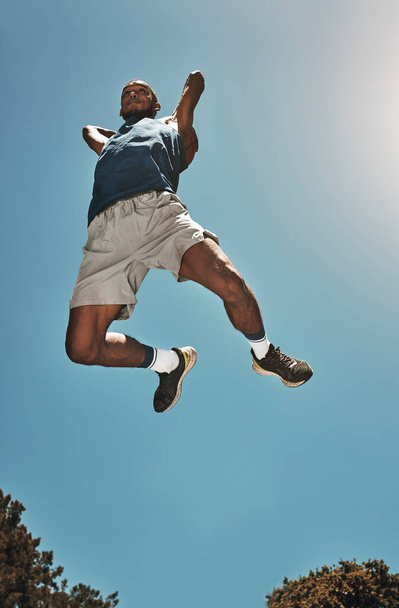 スポーツ、青い空とバスケットボールの男は、ゲーム、競争やスラムダンクトレーニング、練習やワークアウトのためにジャンプします。高エネルギー、選手のモチベーションとフィットネスや運動の下のビューを行うバスケットボール選手. - 写真・画像
