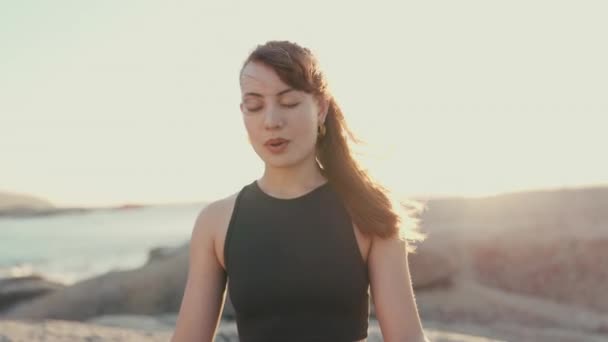 Meditation, peace and breathing with woman at beach for spiritual, mindfulness and fitness. Wellness, freedom and windy with girl relax on rocks in nature for faith, summer break and calm mindset. - Footage, Video