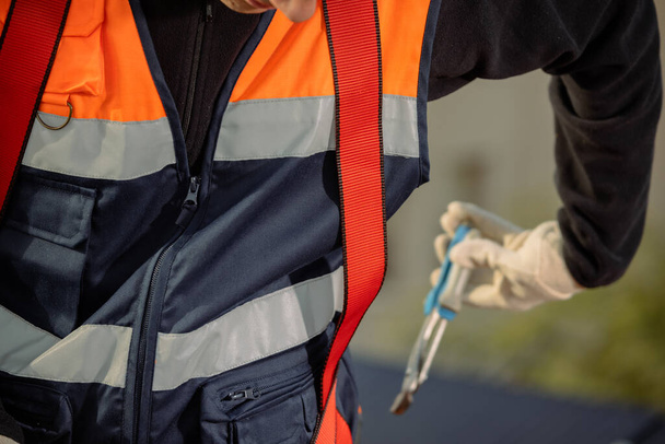 Turuncu yelekli bir elektrikçi işçi kemerinden bir alet alıyor. Yatay - Fotoğraf, Görsel