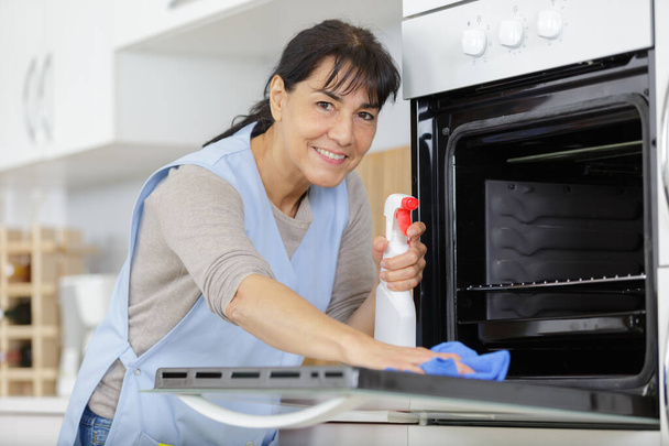 зрелая женщина чистит электрическую печь - Фото, изображение