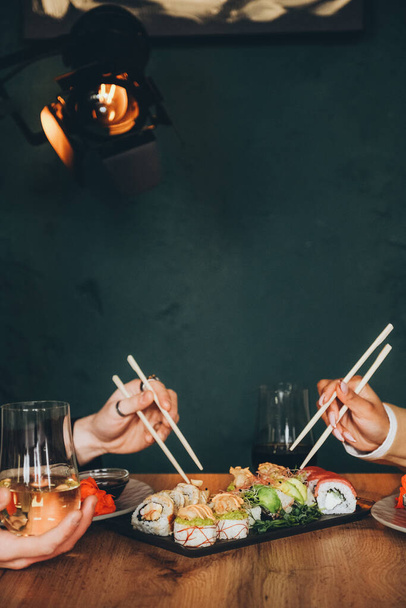 A white man and a black woman eat delicious fresh sushi and drink wine. Lunch at a Japanese restaurant. Asian cuisine. Close-up hands. - Foto, afbeelding