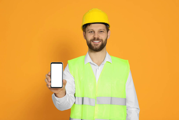 Man in reflective uniform showing smartphone on orange background - Foto, Imagen