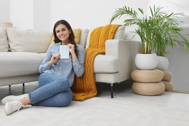 Young woman with greeting card on floor in living room - Photo, image