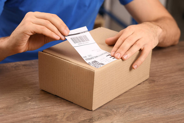 Post office worker sticking barcode on parcel at counter indoors, closeup - Foto, afbeelding