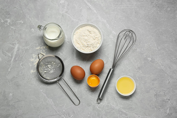 Ingredients for crepes, whisk and sieve on light grey table, flat lay - 写真・画像