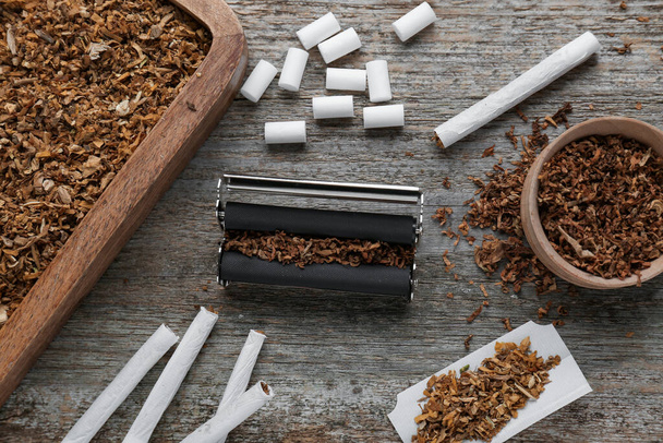 Flat lay composition with roller and tobacco on old wooden table. Making hand rolled cigarettes - Fotografie, Obrázek
