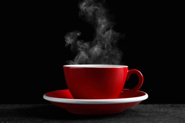 Red cup with hot steaming coffee on dark table against black background - Foto, immagini