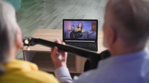 online leren, ouderen paar leren gitaar spelen via video call op laptop met vrouwelijke leraar thuis in de avond - Video