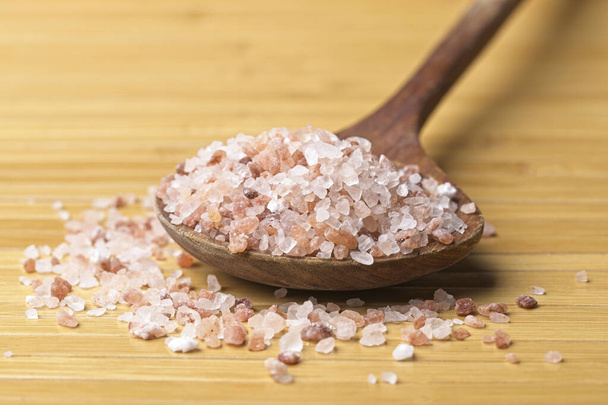 A close up  photo of pink Himalayan sea salt on a wooden spoon and on a table. - Foto, immagini