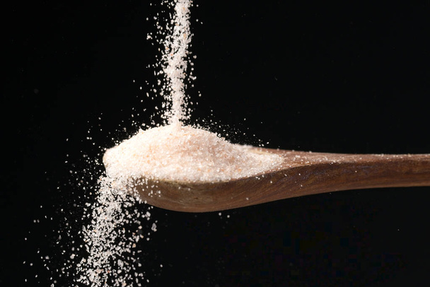 A studio photo of fine himalayan sea salt pouring down on a wooden spoon set against a black background. - Photo, Image