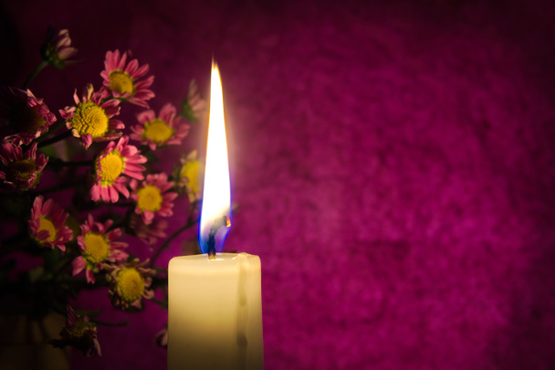 Close up of yellow wax candle flame and flowers illuminated by the candlelight in the dark red background with free copy space - Photo, Image