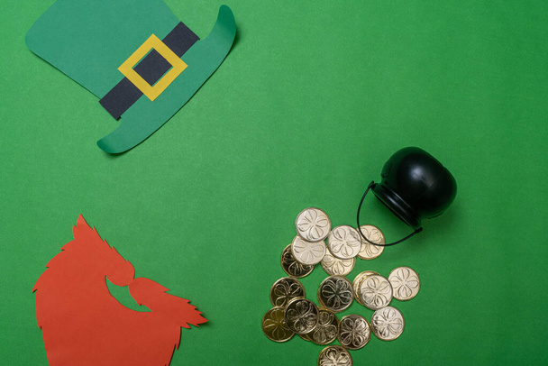 Επίπεδη φωτογραφία για τον εορτασμό της Ημέρας του Αγίου Πατρικίου με καπέλο καλικάτζαρου, πορτοκαλί γενειάδα, μαύρη κατσαρόλα και χρυσά νομίσματα σε πράσινο φόντο - Φωτογραφία, εικόνα