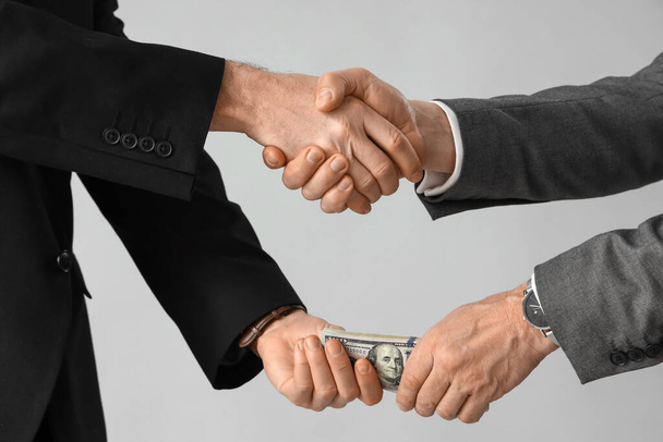 Business men with bribe shaking hands on grey background, closeup - Foto, Imagen
