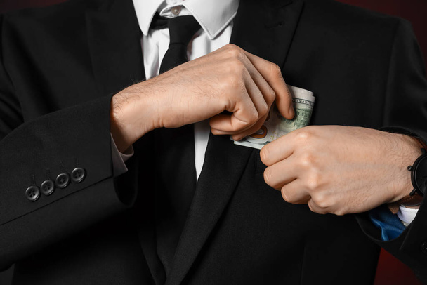 Businessman hiding bribe in pocket on dark background, closeup - Fotoğraf, Görsel