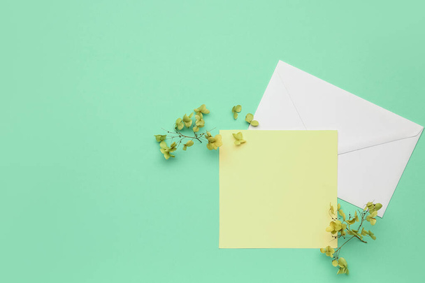Σύνθεση με λευκή κάρτα, φάκελο και αποξηραμένα λουλούδια σε φόντο χρώματος - Φωτογραφία, εικόνα