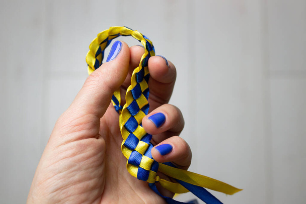 Patriótico amarelo-azul pulseira amuleto artesanato rune trabalho na mão de uma mulher no fundo branco. Um símbolo de independência e apoio aos ucranianos e à Ucrânia na guerra com a Rússia.  - Foto, Imagem