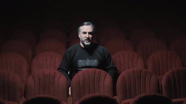Un cantante si siede da solo in un teatro dell'opera vuoto e canta. Un cantante solitario in una sala buia con sedie rosse - Filmati, video