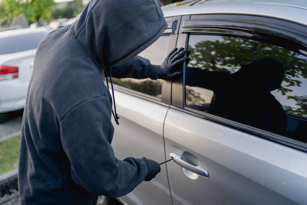 Robber breaking into a car at the parking lot. - Foto, Imagen