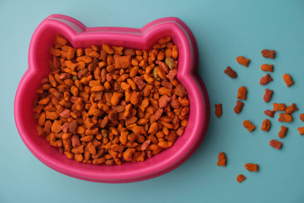 cuenco rosa de comida para gatos sobre un fondo azul, vista superior - Foto, Imagen
