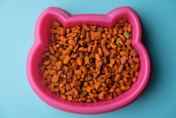 cuenco rosa de comida para gatos sobre un fondo azul, vista superior - Foto, Imagen