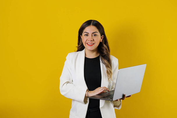 Latin Amerika 'da sarı arka plan üzerinden izole edilmiş dizüstü bilgisayar kullanan genç İspanyol iş kadını. - Fotoğraf, Görsel