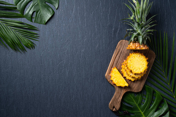 Top view of fresh cut pineapple with tropical leaves on dark blue background. - Foto, afbeelding
