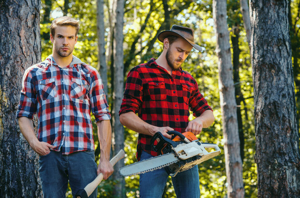 Woodcutters with chainsaw lumberjacks with axe. Hipsters men on serious face with axe. Lumberjack brutal and bearded holds axe. Two lumberjacks in forest. - Φωτογραφία, εικόνα